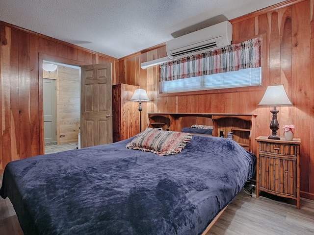 bedroom featuring a textured ceiling, wood walls, light hardwood / wood-style flooring, and a wall mounted air conditioner