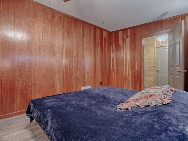 bedroom with a textured ceiling, wood walls, ceiling fan, and light hardwood / wood-style flooring