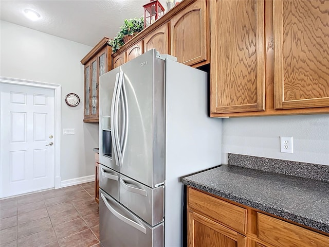 kitchen with stainless steel fridge, light tile patterned flooring, dark stone counters, and a textured ceiling