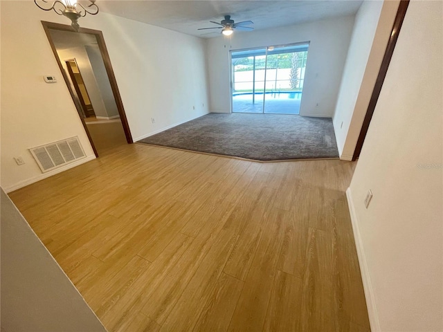 spare room featuring ceiling fan with notable chandelier and light hardwood / wood-style floors