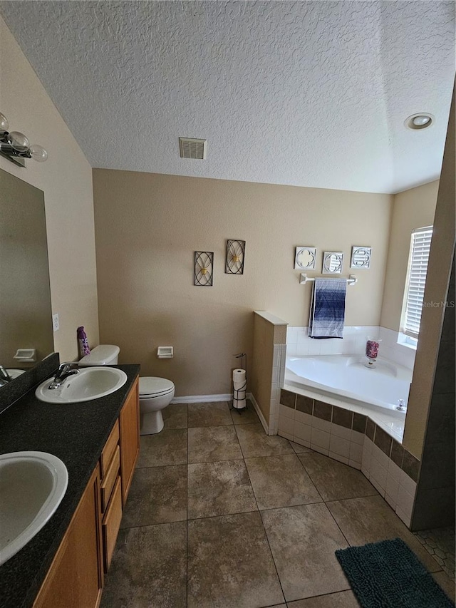 bathroom featuring tiled tub, vanity, a textured ceiling, toilet, and tile patterned floors