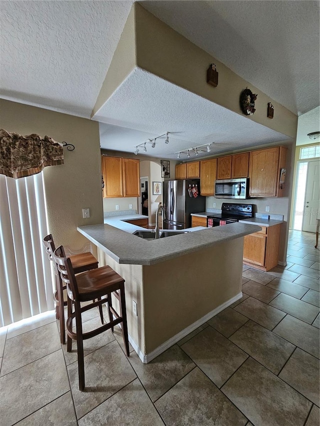 kitchen featuring a textured ceiling, a breakfast bar area, sink, kitchen peninsula, and appliances with stainless steel finishes