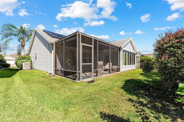 back of property with a sunroom, central AC unit, a lawn, and solar panels