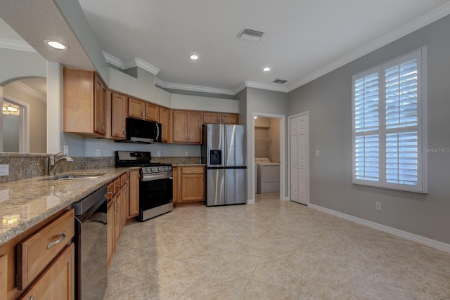 kitchen featuring light stone counters, stainless steel appliances, crown molding, sink, and washing machine and clothes dryer