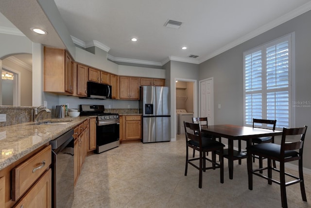 kitchen featuring sink, washer and dryer, ornamental molding, light stone counters, and stainless steel appliances