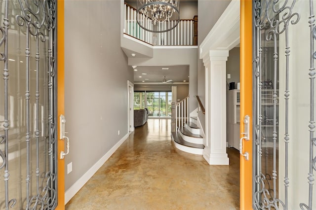 entryway with concrete floors, crown molding, ceiling fan with notable chandelier, a towering ceiling, and ornate columns