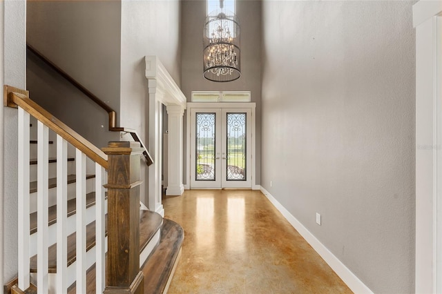 foyer entrance featuring french doors, a chandelier, concrete flooring, a towering ceiling, and ornate columns