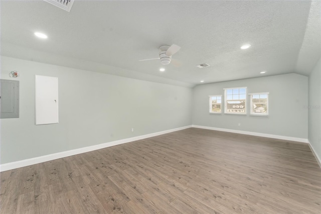 spare room featuring lofted ceiling, electric panel, light wood-type flooring, and a textured ceiling