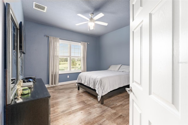 bedroom with ceiling fan, light hardwood / wood-style floors, and a textured ceiling