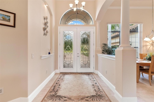 tiled foyer featuring french doors, ornate columns, crown molding, and a chandelier