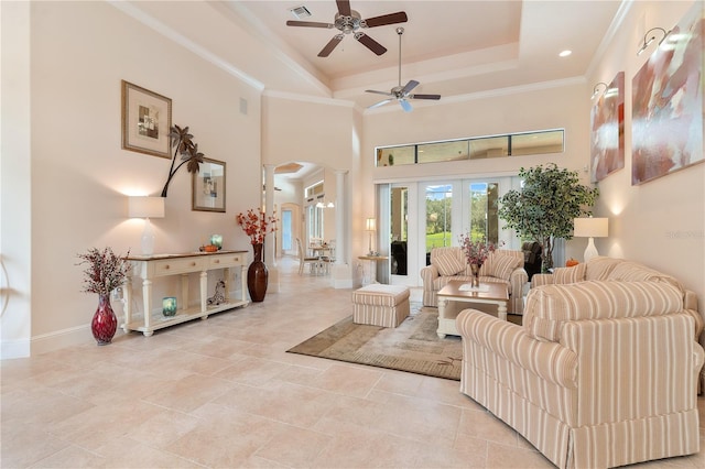 living room with a raised ceiling, ceiling fan, ornamental molding, ornate columns, and a towering ceiling