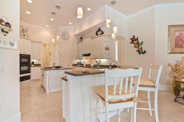 kitchen with kitchen peninsula, a kitchen bar, pendant lighting, double oven, and a center island