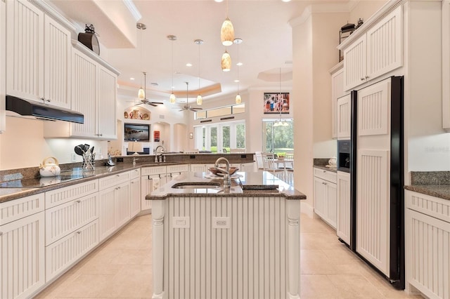 kitchen featuring paneled built in fridge, decorative light fixtures, kitchen peninsula, and a center island with sink