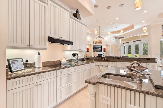 kitchen featuring black electric cooktop, kitchen peninsula, dark stone countertops, sink, and decorative light fixtures