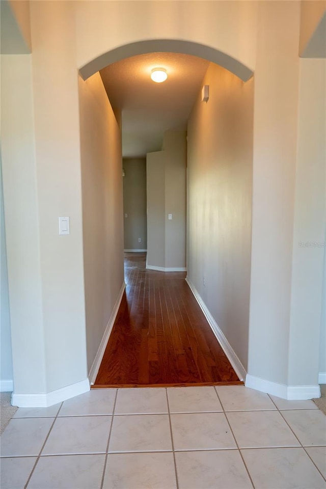 hallway featuring tile patterned flooring, baseboards, and arched walkways