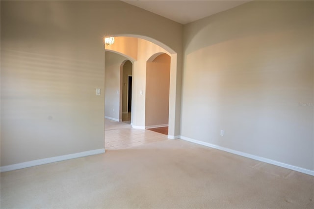 unfurnished room with light tile patterned floors, baseboards, light carpet, and arched walkways