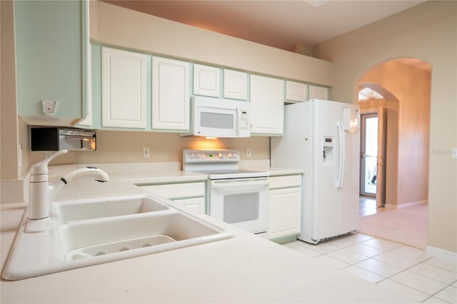 kitchen with light tile patterned flooring, arched walkways, white appliances, white cabinetry, and a sink