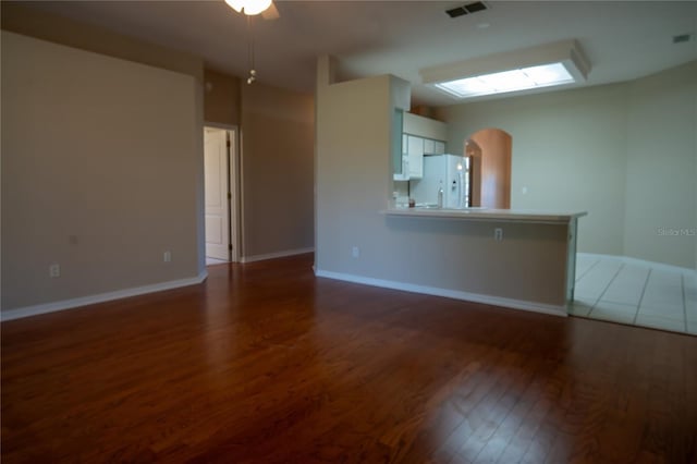 unfurnished living room with visible vents, arched walkways, baseboards, and wood finished floors