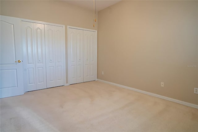 unfurnished bedroom with baseboards, two closets, and carpet flooring