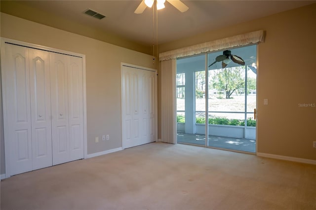 unfurnished bedroom featuring baseboards, visible vents, carpet floors, ceiling fan, and multiple closets