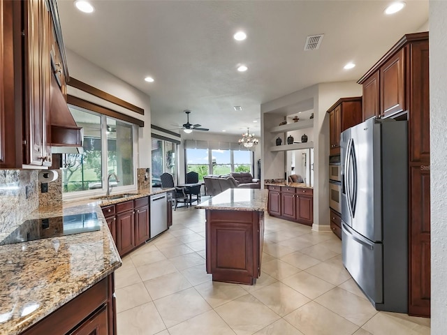 kitchen with a kitchen island, appliances with stainless steel finishes, sink, ceiling fan with notable chandelier, and light stone counters