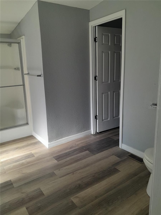 bathroom with toilet, wood-type flooring, and a shower with door