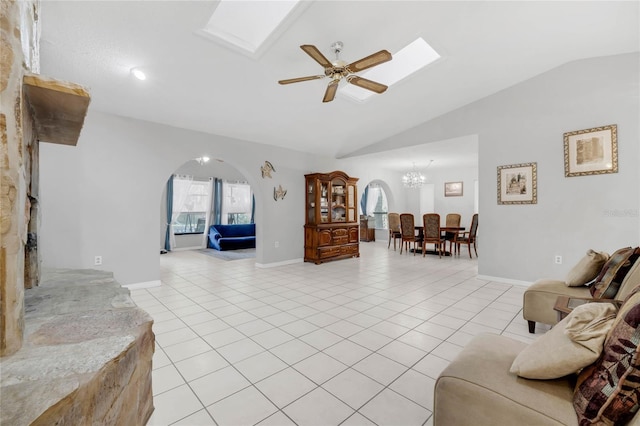 tiled living room with ceiling fan with notable chandelier and lofted ceiling with skylight