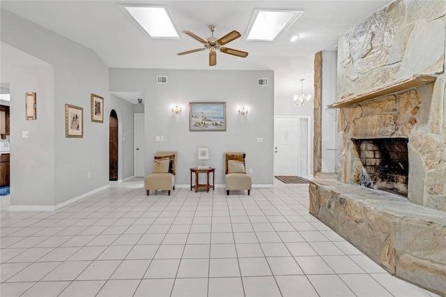 interior space with a stone fireplace, a skylight, ceiling fan with notable chandelier, and light tile patterned floors