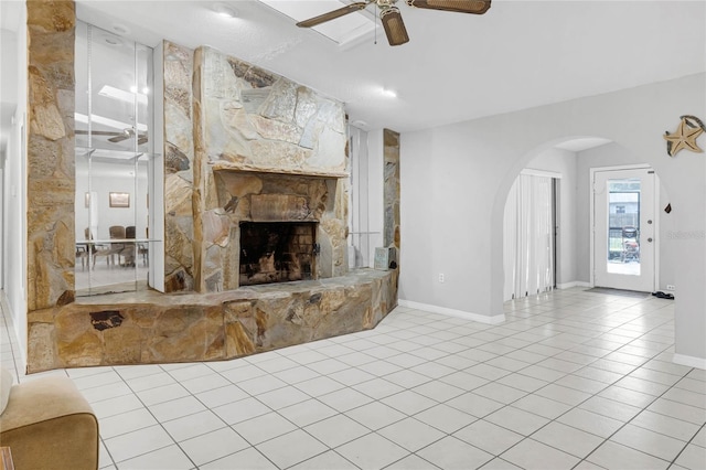 living room featuring ceiling fan, light tile patterned floors, and a stone fireplace