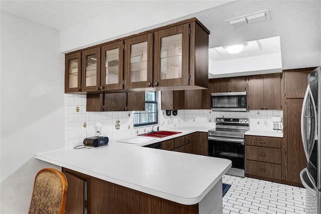 kitchen with sink, kitchen peninsula, tasteful backsplash, a textured ceiling, and appliances with stainless steel finishes