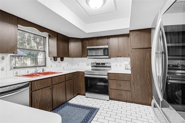 kitchen featuring appliances with stainless steel finishes, backsplash, a raised ceiling, dark brown cabinets, and sink