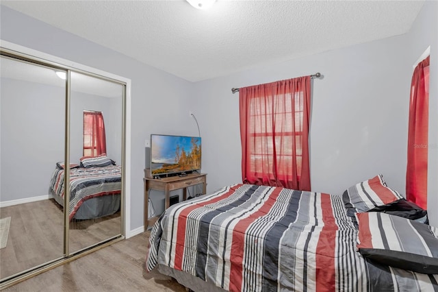 bedroom with light wood-type flooring, a textured ceiling, multiple windows, and a closet