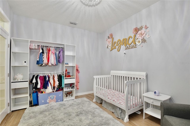 bedroom featuring a textured ceiling, a crib, and hardwood / wood-style floors