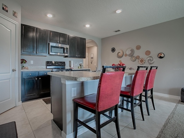 kitchen featuring a kitchen breakfast bar, a center island with sink, black electric range oven, and a textured ceiling