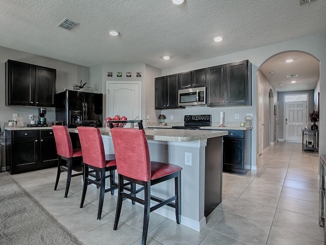 kitchen featuring black appliances, a kitchen breakfast bar, light tile patterned floors, an island with sink, and a textured ceiling