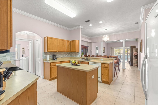 kitchen with white appliances, a center island, decorative light fixtures, ornamental molding, and washer and dryer