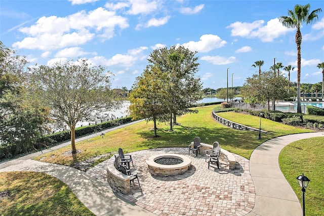 surrounding community with a water view, a fire pit, and a lawn