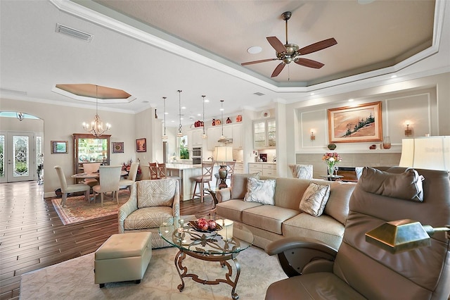 living room with ceiling fan with notable chandelier, a raised ceiling, and ornamental molding