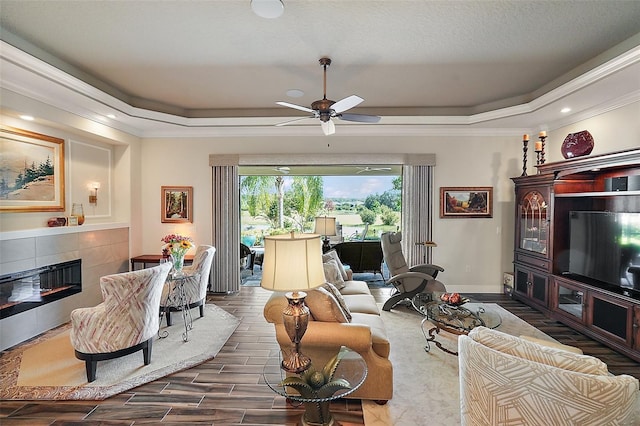 living room featuring ceiling fan, crown molding, a tile fireplace, and a tray ceiling