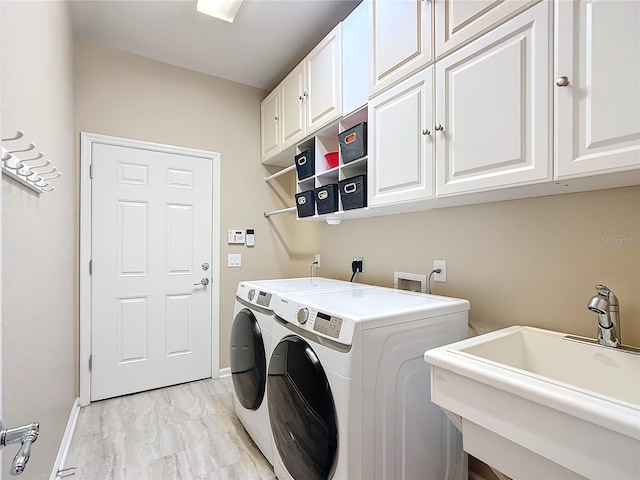 clothes washing area with sink, washing machine and clothes dryer, and cabinets