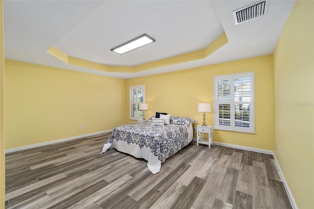 bedroom with wood-type flooring and a tray ceiling