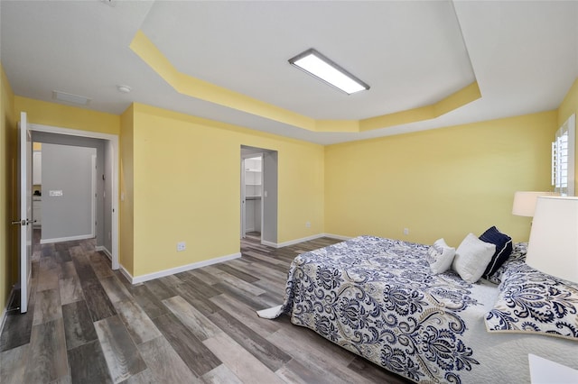 bedroom featuring a walk in closet, hardwood / wood-style floors, a closet, and a tray ceiling