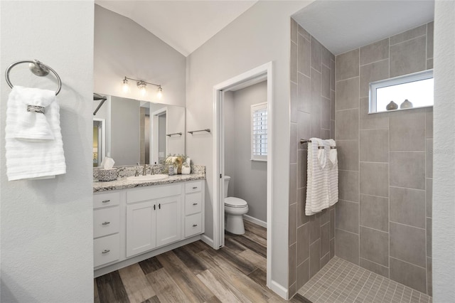 bathroom featuring wood-type flooring, toilet, lofted ceiling, tiled shower, and vanity