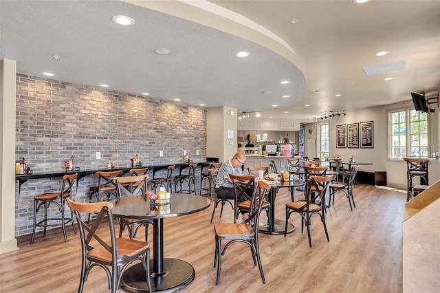 dining area with light hardwood / wood-style flooring, a textured ceiling, brick wall, and bar