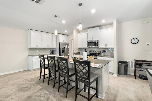 kitchen featuring white cabinets, a center island with sink, appliances with stainless steel finishes, and decorative light fixtures