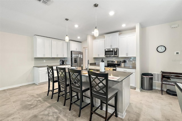 kitchen with a breakfast bar area, an island with sink, a sink, appliances with stainless steel finishes, and decorative backsplash