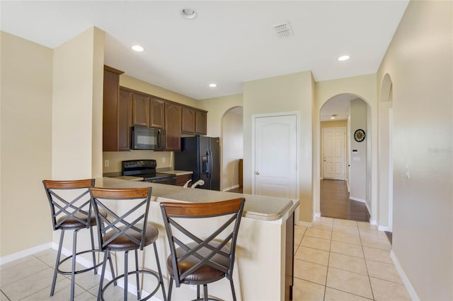 kitchen with kitchen peninsula, dark brown cabinets, black appliances, a breakfast bar area, and light tile patterned flooring