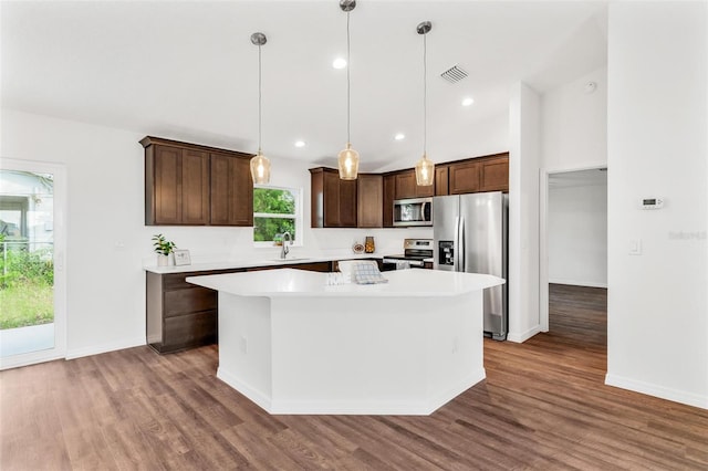 kitchen with dark hardwood / wood-style flooring, appliances with stainless steel finishes, a kitchen island, sink, and decorative light fixtures