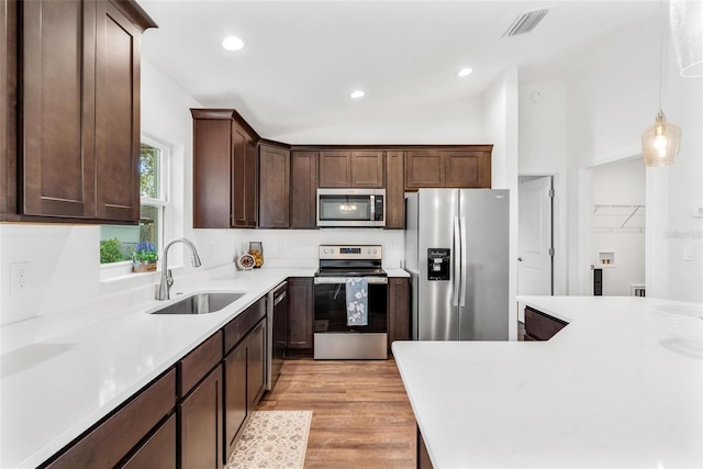 kitchen featuring lofted ceiling, hanging light fixtures, light wood-type flooring, sink, and stainless steel appliances