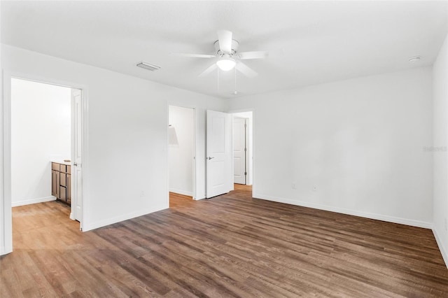 unfurnished bedroom with ensuite bath, hardwood / wood-style floors, a walk in closet, and ceiling fan